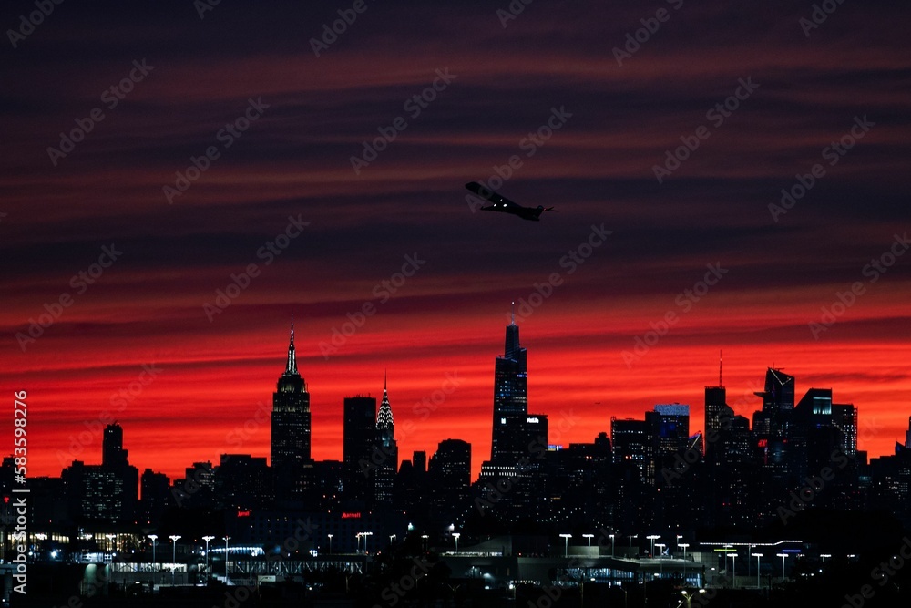Beautiful view of a plane flying over the night skylines of NYC on a sunset sky background