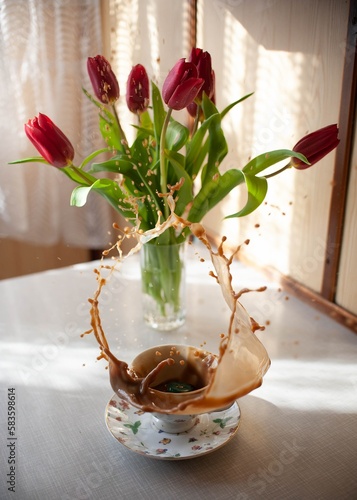 cup of coffee splashing, jumping, next to flowers