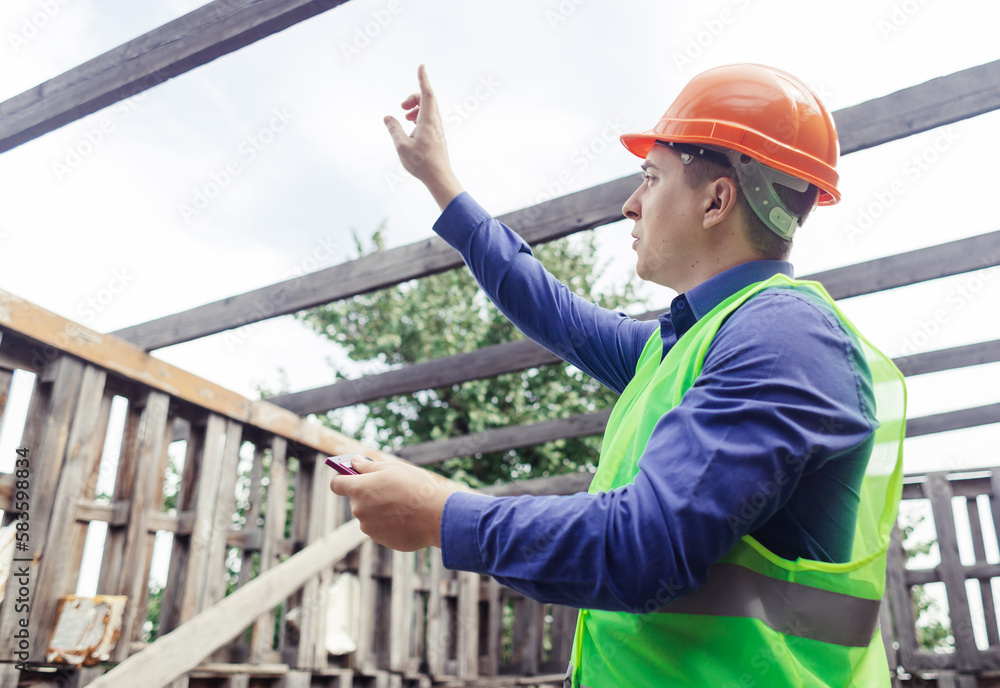 Building inspector. Man in a hard hat and a yellow reflective vest examines damaged structures and inspects the building. Damage assessment. Preparing for the repair or construction of a building Building inspector. Man in a hard hat and a yellow reflective vest examines damaged structures and inspects the building. Damage assessment. Preparing for the repair or construction of a building
