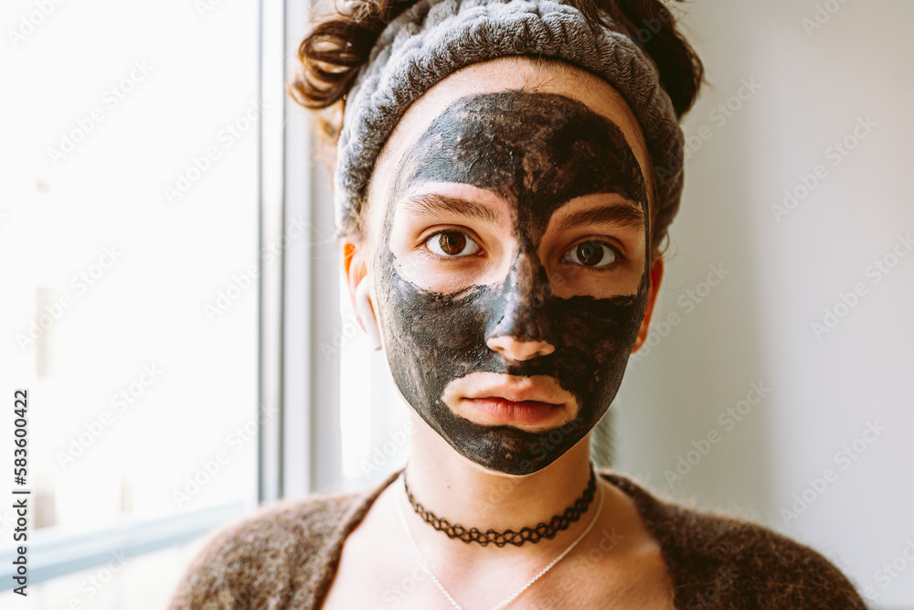Young woman with black cosmetic mask on her face at home. Skin care. Young woman with black cosmetic mask on her face at home. Skin care.