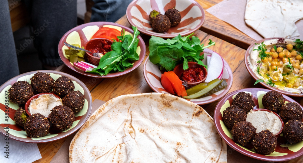 High angle view on a set of Middle East dishes on a wooden table. Pita bread, falafel balls, humus and vegetables. Fresh vegan food. High angle view on a set of Middle East dishes on a wooden table. Pita bread, falafel balls, humus and vegetables. Fresh vegan food.