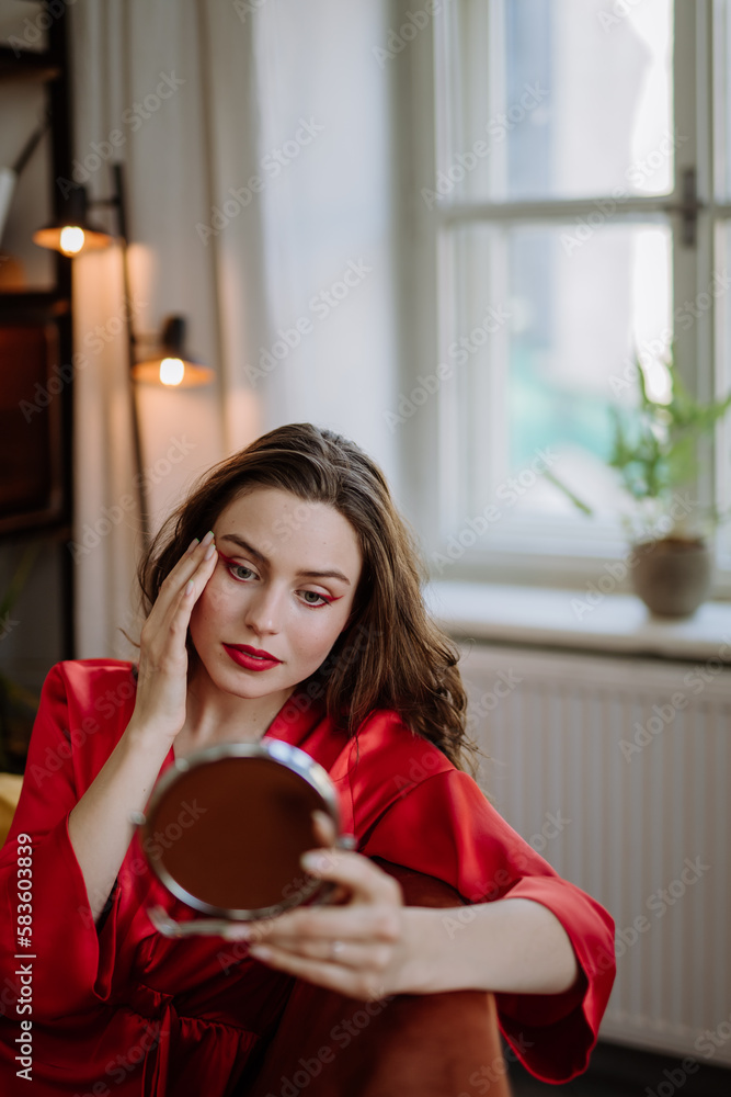 Young woman in elegant dress preparing for evening, finishing her make up.