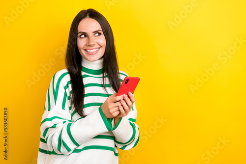 Photo of cheerful dreamy lady dressed striped pullover texting modern gadget looking empty space isolated yellow color background
