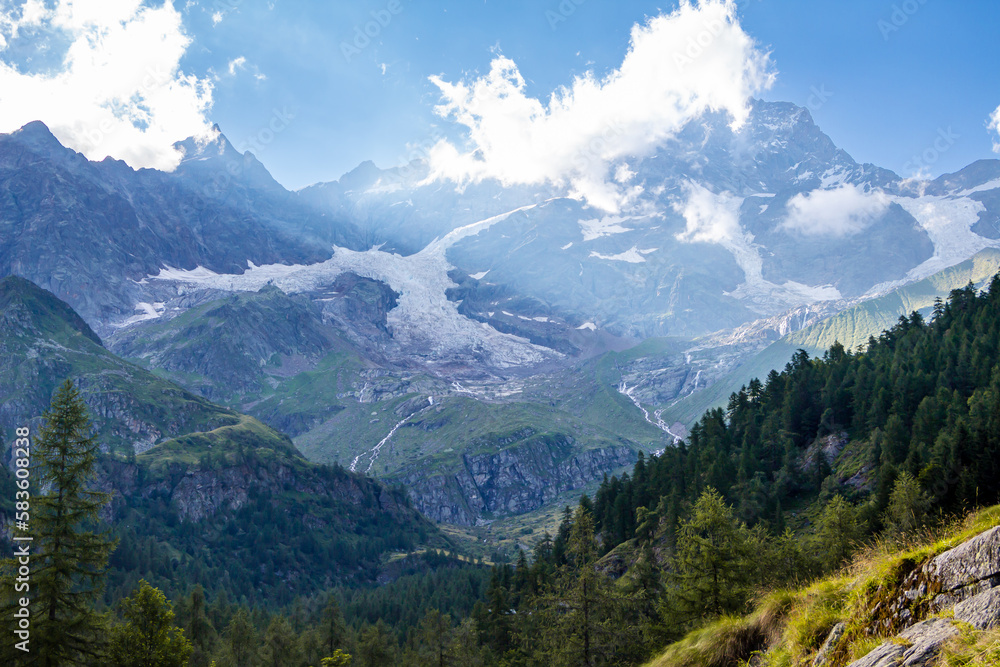 Panorama along the path in the Alta Valsesia Natural Park in summer. Trekking in the mountains. View of the peaks, meadows, trees and woods and sky. Italian Alp. Alagna Valsesia. Piedmont. Alps Italy Panorama along the path in the Alta Valsesia Natural Park in summer. Trekking in the mountains. View of the peaks, meadows, trees and woods and sky. Italian Alp. Alagna Valsesia. Piedmont. Alps Italy