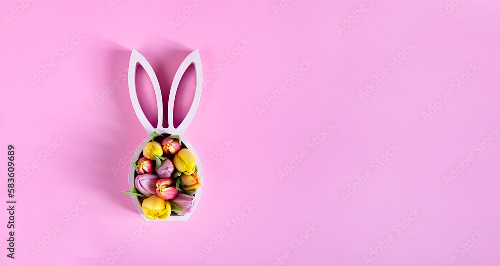 Wooden easter bunny statuette with spring tulips on the pink background, easter minimal concept, top view with copy space