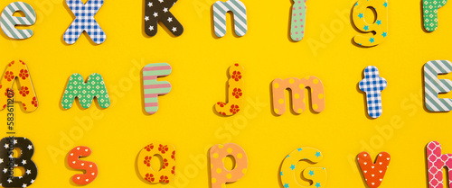 Many multi-colored letters of the alphabet on a yellow background. Top view  flat lay. Banner