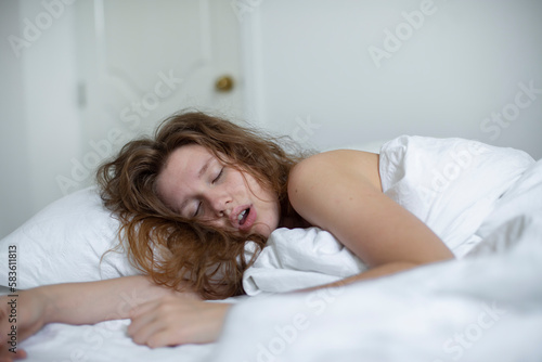 young girl sleeps in the morning in bed and snores loudly with her mouth open, the concept of person have problem with sleep and breathing photo