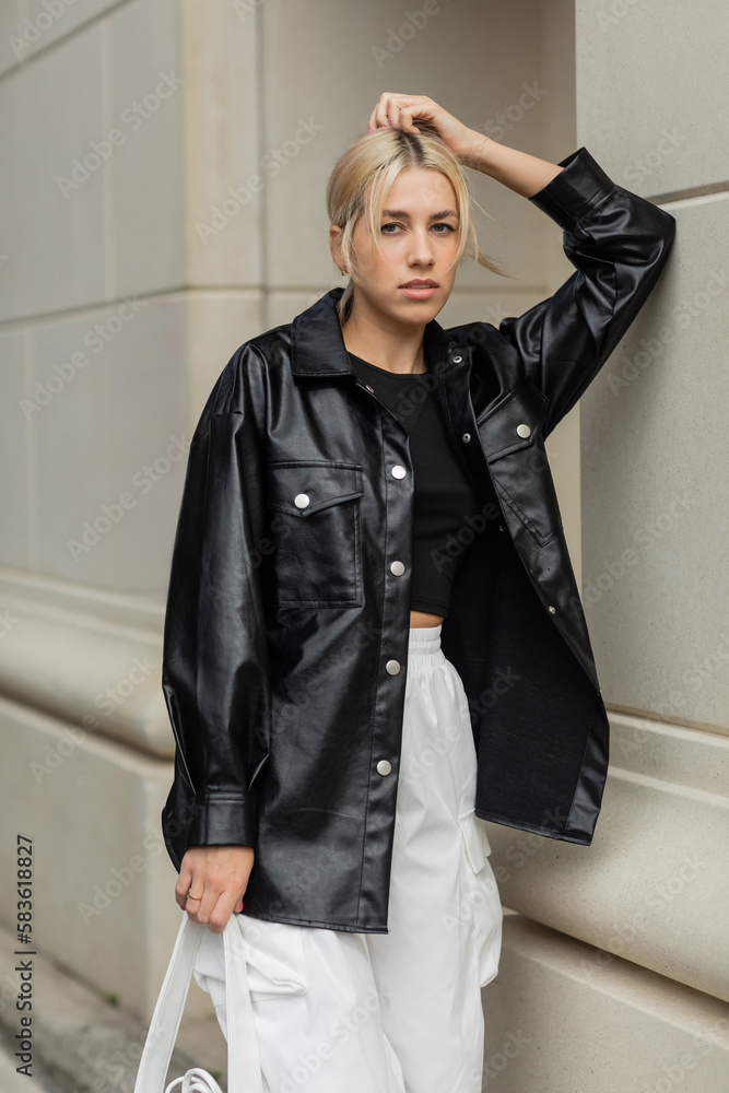 blonde woman in leather shirt jacket posing with handbag on street in Miami. blonde woman in leather shirt jacket posing with handbag on street in Miami.