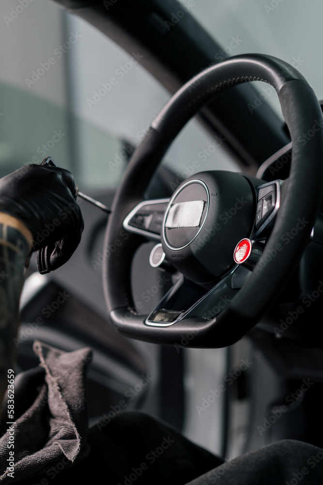 A mechanic in gloves cleans the steering wheel with a microfiber cloth and blows dust with a special tool