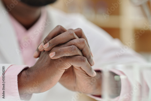 Close-up of clasped hands of young African American male clinician wearing lab coat concentrating while thinking during work