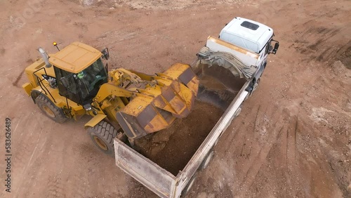 Bucket loader loading soil onto a truck trailer, Top down view
