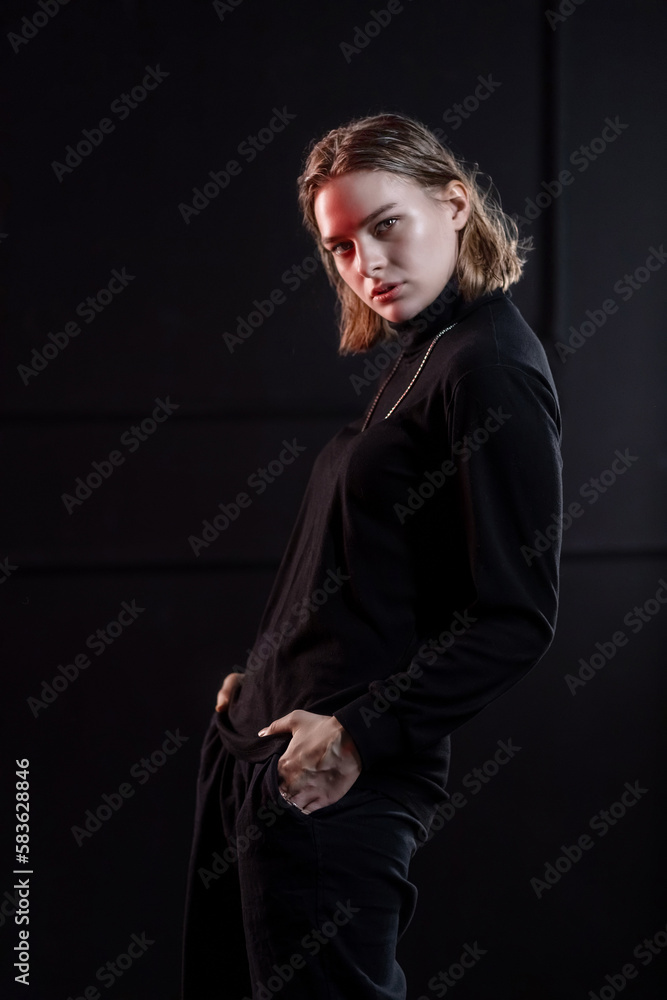 A slender, beautiful young girl in black clothes poses in a neon red-blue light on a black background.Black on black. Neon A slender, beautiful young girl in black clothes poses in a neon red-blue light on a black background.Black on black. Neon