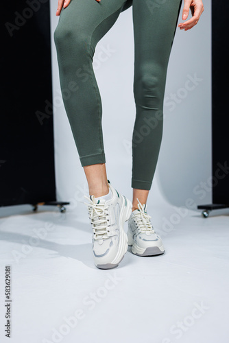 Slender female legs in leggings and white stylish casual sneakers. Women's comfortable summer shoes.