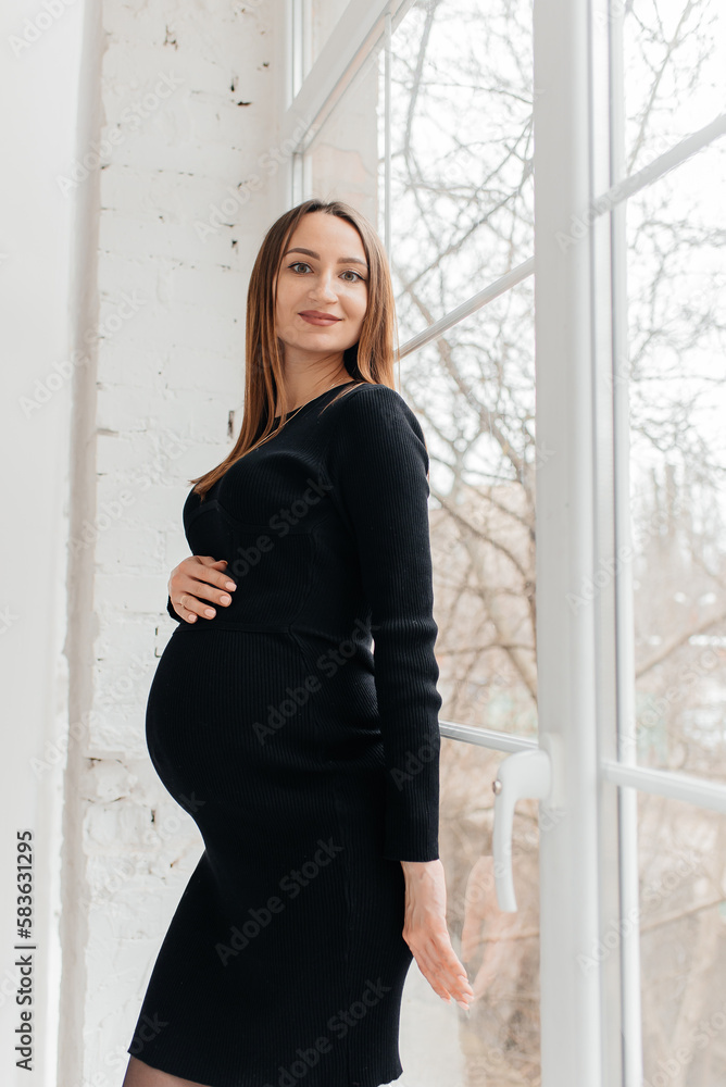 Beautiful young pregnant woman in black dress posing in hall Beautiful young pregnant woman in black dress posing in hall