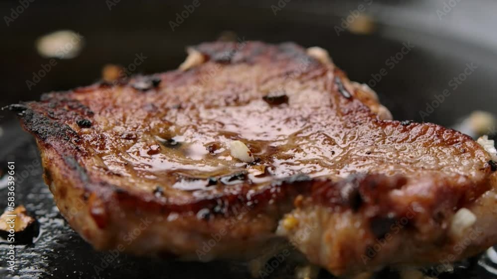 Pieces of garlic fall in slow motion onto a fried steak in a pan Pieces of garlic fall in slow motion onto a fried steak in a pan