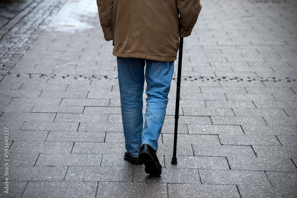 Closeup of legs of old man waking in the street with stick