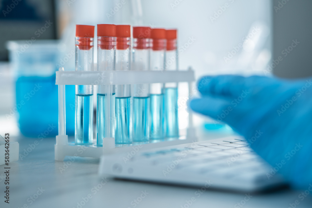 A female researcher sits at a workplace in a laboratory, behind a personal computer monitor. Against the background research statistics. Pharmaceutical medical worker in protection works at keyboard. A female researcher sits at a workplace in a laboratory, behind a personal computer monitor. Against the background research statistics. Pharmaceutical medical worker in protection works at keyboard.