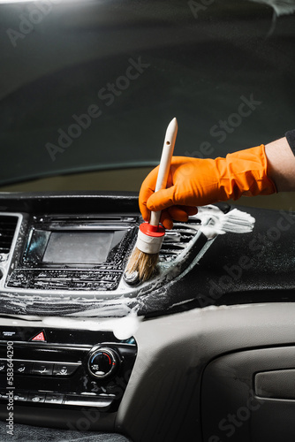 Cleaning with brush and detergent of air dashboard and multimedia in the car. Worker in detailing auto service clean elements of interior of car. photo