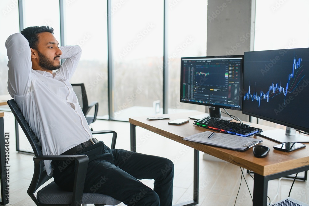 Side view of smart Indian crypto trader, investor, analyst broker, using laptop and smartphone analyzing digital cryptocurrency exchange, stock market charts, thinking of investing and funds risks. Side view of smart Indian crypto trader, investor, analyst broker, using laptop and smartphone analyzing digital cryptocurrency exchange, stock market charts, thinking of investing and funds risks.