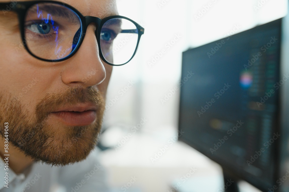 Young business man trader wearing glasses looking at computer screen with trading charts reflecting in eyeglasses watching stock trading market financial data growth concept, close up. Young business man trader wearing glasses looking at computer screen with trading charts reflecting in eyeglasses watching stock trading market financial data growth concept, close up.