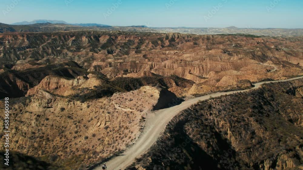 Cinematic aerial shot of Sierra Nevada desert in the summer heat. Female cyclist riding a bike trough stunning scenery. Outdoor adventure. Peaceful escape and challenging workout. Goal achievement. Cinematic aerial shot of Sierra Nevada desert in the summer heat. Female cyclist riding a bike trough stunning scenery. Outdoor adventure. Peaceful escape and challenging workout. Goal achievement.