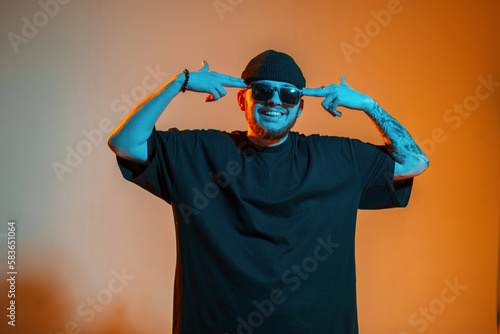 Cool funny happy handsome man with trendy fashion sunglasses in stylish black t-shirt posing in creative studio with orange and neon light