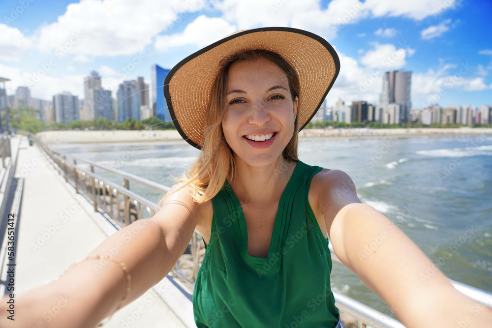 Beautiful girl takes selfie picture with modern skyscrapers skyline on the ocean