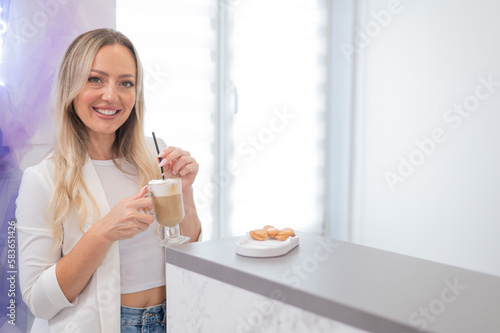 Female client of a beauty salon drinking coffee at the reception desk. 