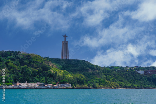 Lisbon, Portugal day sea view of Cristo Rei statue, Christ the King Sanctuary, against blue sky with clouds over the Tagus River.