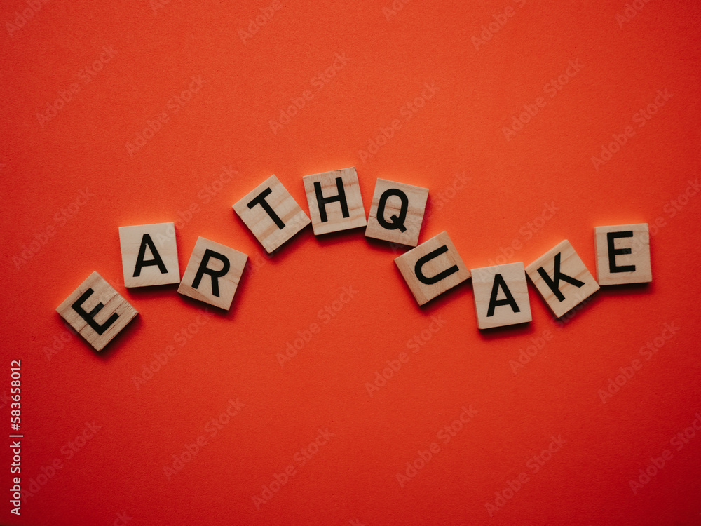 Obraz premium Inscription earthquake from vibration moves on background. Concept of earthquake, destruction and shifts of earth's crust. Wooden square blocks with letters are laid out on orange sheet. Slow motion