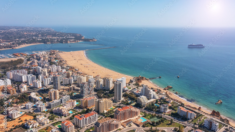 Aerial view of Portuguese city of Portimao with buildings on coast with beaches. Tourist cruise liner in the background in the sea.