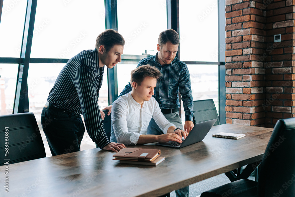 Three men working together on laptops in a modern office space. Young