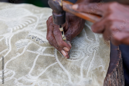 Male fingers holding an awl and hammer, punching holes in leather, creating an elephant design. Leatherwork 