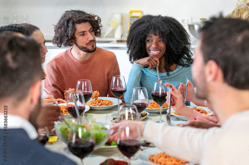 Multiethnic friends eat spaghetti with tomato sauce together in the kitchen of a shared apartment Multiethnic friends eat spaghetti with tomato sauce together in the kitchen of a shared apartment