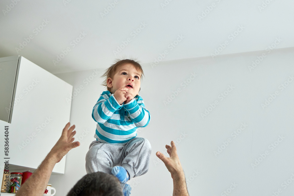 Young dad throwing excited laughing baby boy up in air and catching