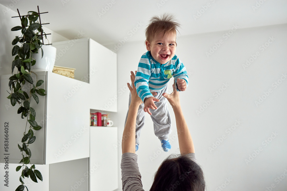 Young mom throwing excited laughing baby boy up in air and catching