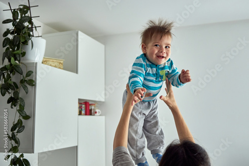 Young mom throwing excited laughing baby boy up in air and catching