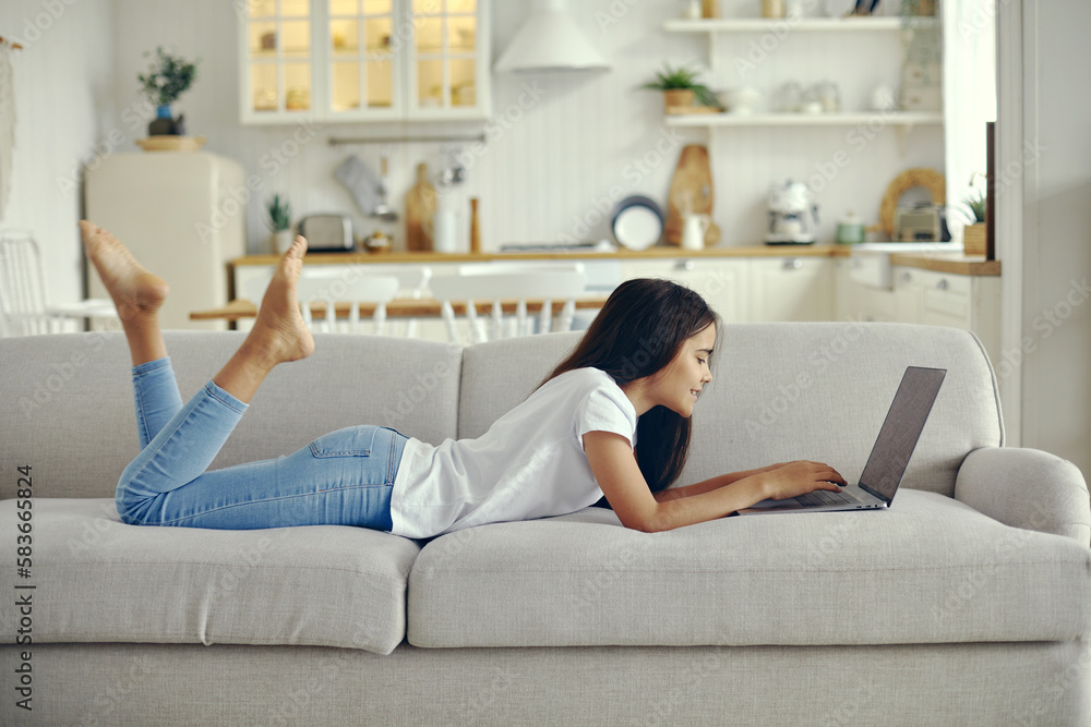 Cute preteen 12s girl use laptop lying on couch Stock Photo | Adobe Stock