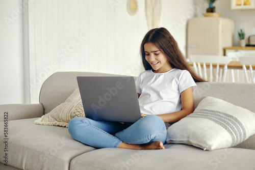 Cute 12s girl use laptop sit on sofa in living room