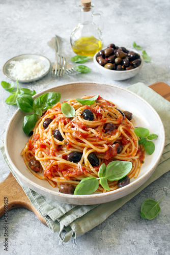 Pasta with tomato sauce, dark olive and parmesan cheese on light background. Spaghetti alla puttanesca. Top view.