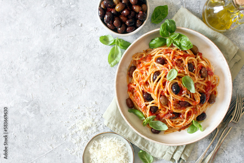 Pasta with tomato sauce, dark olive and parmesan cheese on light background. Spaghetti alla puttanesca. Top view.