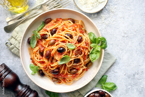 Pasta with tomato sauce, dark olive and parmesan cheese on light background. Spaghetti alla puttanesca. Top view.