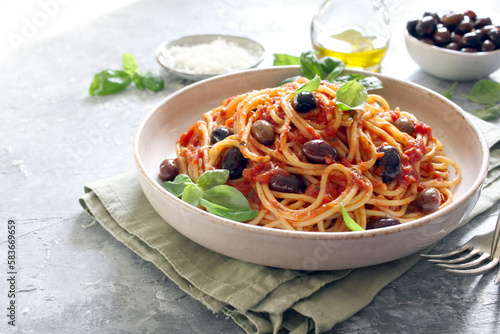 Pasta with tomato sauce, dark olive and parmesan cheese on light background. Spaghetti alla puttanesca. Top view.