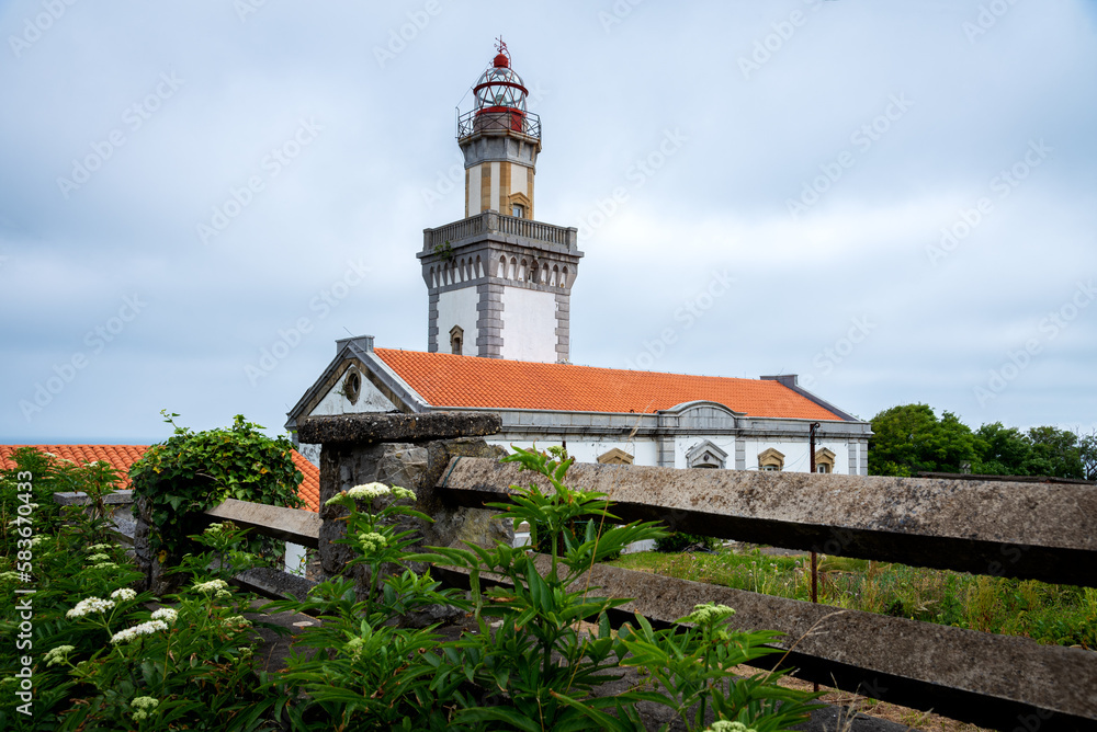 Higuer lighthouse surrounded by green vegetation. Building against a cloudy and stormy sky, Hondarribia, Guipuzcoa, Basque Country, Spain