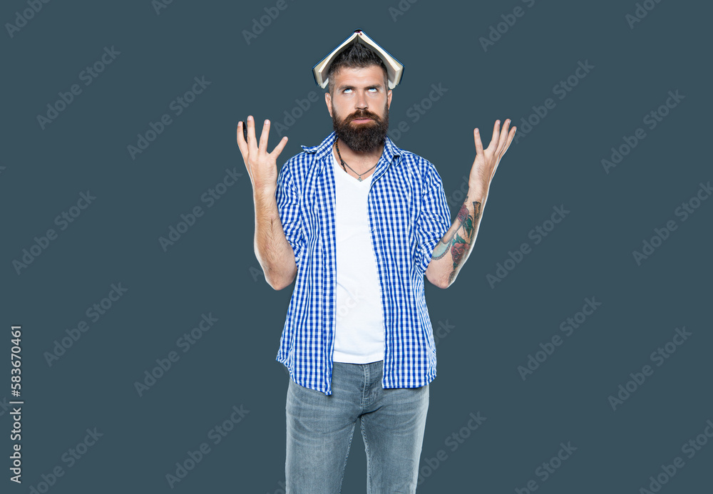 Fototapeta premium irritated bearded man with book on head on grey background