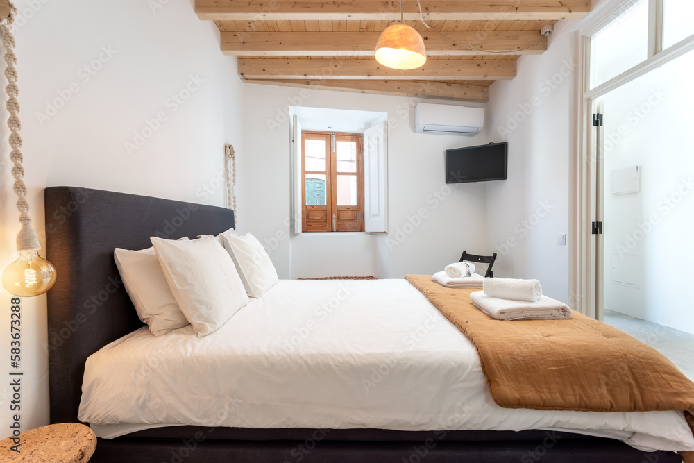 Traditional modern Iberian bedroom with wooden ceiling and clean towels and linens.