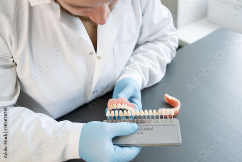 Dental technician hold palette of shades of teeth scale. 