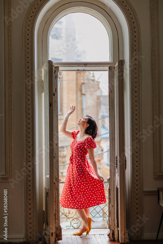 a beautiful and happy brunette women in red retro dress in the balcony doorway 
