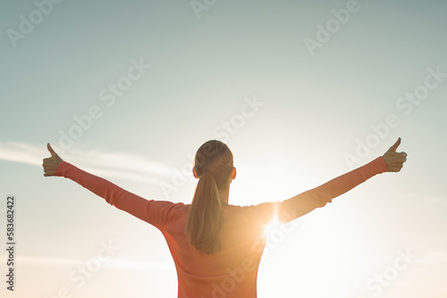 Having a positive mindset, wellbeing and hope concept. Happy young woman standing in a nature sunrise with arms outstretched. 