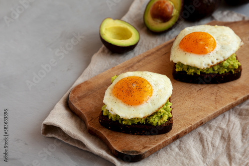 Homemade Avocado Toast with Eggs on a rustic wooden board, side view. Space for text.